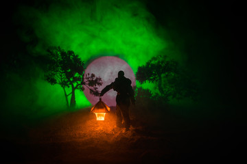 Man in raincoat coming from dark forest with glowing lantern in his hand concept. Silhouette of a...