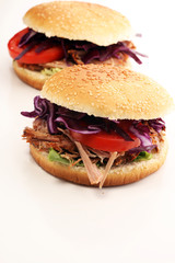 Pulled pork sandwiches with BBQ sauce, cabbage and tomato on table
