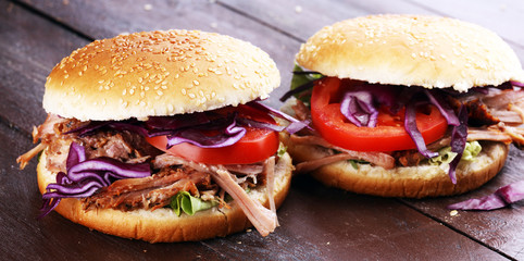 Pulled pork sandwiches with BBQ sauce, cabbage and tomato on table