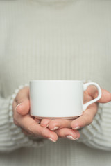 Girl in warm sweater is holding white mug in hands.. Mockup for winter gifts design.