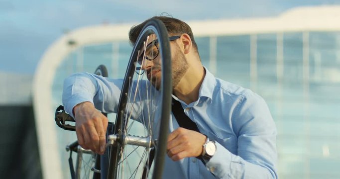 Close up of the attractive young man in the casual style repairing his bike while scewing the wheel at the big city building background.