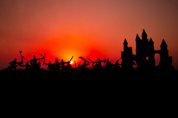 Medieval battle scene with cavalry and infantry. Silhouettes of figures as separate objects, fight between warriors on sunset foggy background.