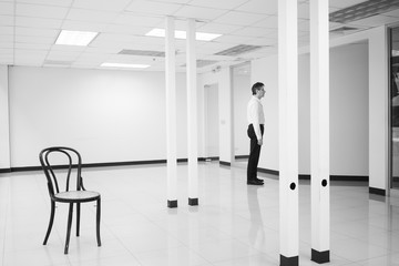 Businessman standing in empty bright office and look at wall thinking
