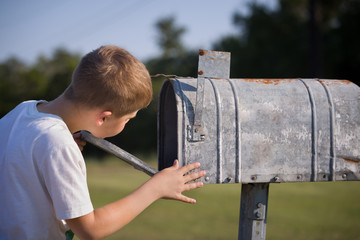 A cute boy, checking the mail in an open mail box. The kid is waiting for the letter, checks the...