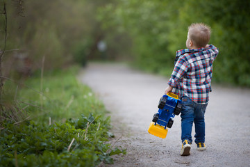Cute kid boy is walking in the garden with a colourful tractor in his hand. © goodmoments