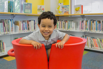 A happy little boy sits in two red U-shape chairs pushed together.