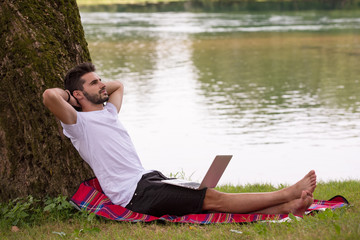 man using a laptop computer on the bank of the river