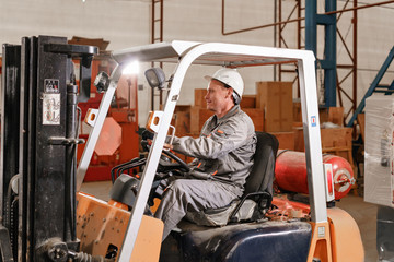 Fototapeta na wymiar close - up steering wheel and levers. man driving a forklift through a warehouse in a factory. driver in uniform and protective helmet. the concept of logistics and storage