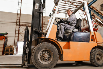man driving a forklift through a warehouse in a factory. driver in uniform and protective helmet. the concept of logistics and storage