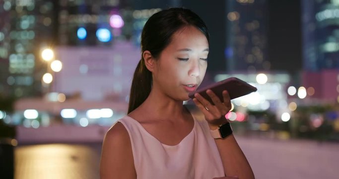 Woman sending on audio message on cellphone at night