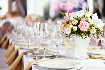 Table at a luxury wedding reception. Beautiful flowers on the table. Serving dishes, glass glasses, waiters work,