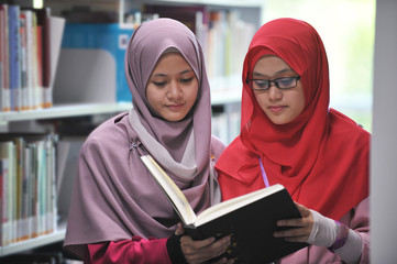 Two young beautiful muslimah student discussing in the library.