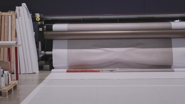 Industrial Big Printer, professional press, and paper supply. Robotized workflow, detailed shot of the passing print head, while processing large, vinyl, glossy, rolls. Color samples before final ok.