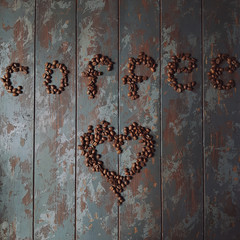 Fresh roasted coffee beans on rustic wooden table in shape of heart and word coffee, top view
