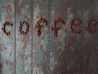 Fresh roasted coffee beans on rustic wooden table in shape of heart and word coffee, top view, space for text
