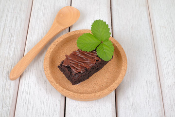 Wooden spoon and chocolate brownie with melted chocolate on a wooden plate