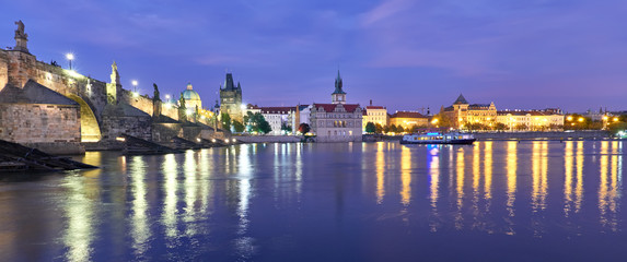 Illuminated Charles Bridge is reflected in Vltava river at night in Prague, panorama