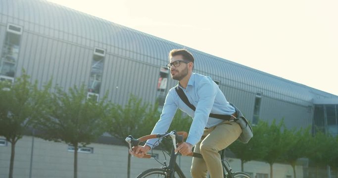 Portrait shot of the young attractive Caucasian businessman coming back home from work on the bicycle on a sunny day.
