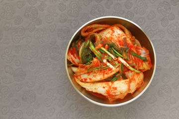 The most famous Korean food Kimchi(geotjeori, fresh vegetable salad) in traditional brassware on silk pattern background. Top view. 