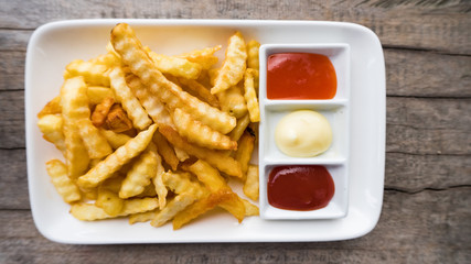 French fries in a white dish with ketchup and chili sauce on wooden floor.