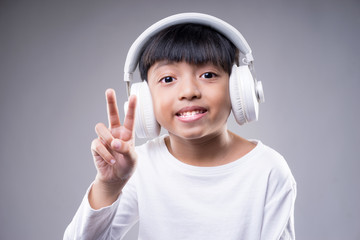 Asian boy wearing a wireless headphone and enjoying music on a grey background.
