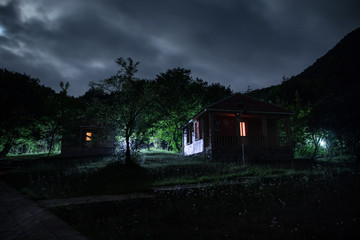 Mountain night landscape of building at forest at night with moon or vintage country house at night with clouds and stars. Summer night.