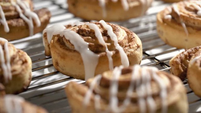 Cinnamon bun on cooling rack with white icing being dripped over the fresh baked pastries. 
