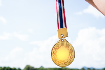 Winner hand raised holding gold medals with Thai ribbon against blue sky. Golden medals is award for highest achievement for sport or business. Success Awards concept
