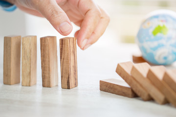 Strategy planning risk in business concept : Businessman or engineer placing wooden block dominos on table with blur global model. Alternative risk for goal and success