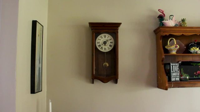 Wide shot of clock ticking on wall near next to shelf during the day.
