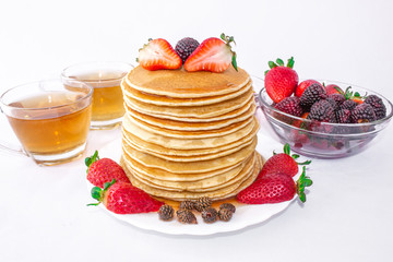Delicious breakfast. Pancakes with fruit, strawberries and blackberries (mora) pour syrup (honey) on a white background. Two cups of tea.