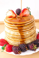 Tasty breakfast. Pancakes with fruit, strawberries and blackberries (mora) pour syrup (honey) on a white background. Close-up.