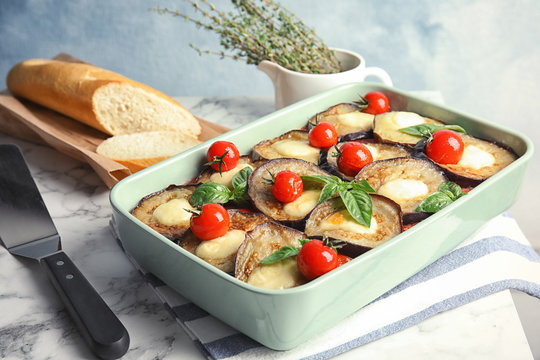 Baked eggplant with tomatoes, cheese and basil in dishware on marble table