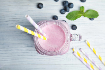 Mason jar of tasty milk shake and blueberries on wooden background, top view