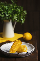 Plate with ripe corn cobs on table against dark background. Space for text
