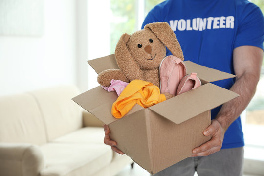 Male volunteer holding box with donations indoors. Space for text