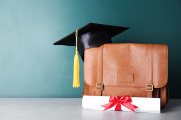 Graduation hat with briefcase and diploma on table near chalkboard. Space for text
