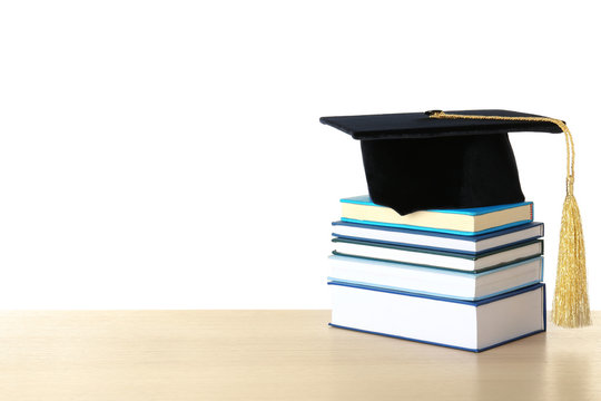 Graduation hat with books on table against white background