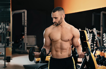 Fototapeta na wymiar Strong young man lifting dumbbells in gym