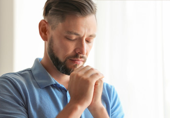 Fototapeta na wymiar Man with hands clasped together for prayer on light background. Space for text