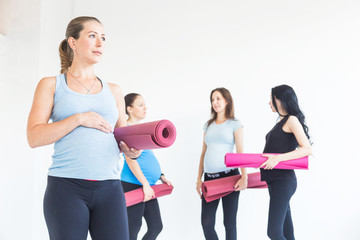 pregnancy, sport, fitness, people and healthy lifestyle concept - group of happy pregnant women exercising yoga and and meditating in lotus pose in white background gym