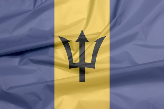 Fabric flag of Barbados. Crease of Barbadian flag background, triband of ultramarine (hoist-side and fly-side) and gold with the black trident-head centred on the gold band.