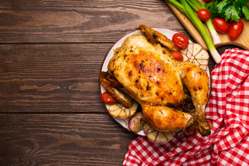 Baked chicken or turkey with garlic cloves and vegetables served on a plate. Wooden background. Copy space. Flat layout