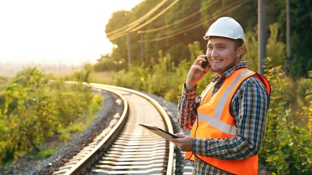 Happy railway employee with a phone and a notebook on the railroad, reports the result of the check