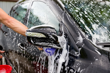 Cleaning automobile Using High Pressure Water. Man washing his car under high pressure water in service.worker washing car.Protection of car concept.male hand with purpl sponge washing auto.Selective