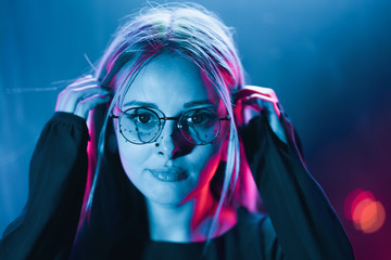 Millennial enigmatic pretty girl with unusual dyed hairstyle near glowing neon wall at night. Blue...