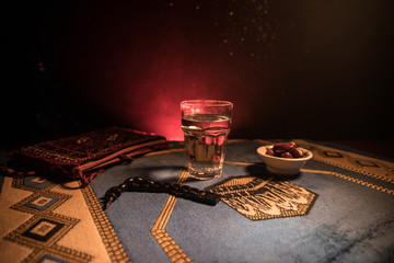Water and dates. Iftar is the evening meal. View of decoration Ramadan Kareem holiday on carpet. Festive greeting card, invitation for Muslim holy month Ramadan Kareem. Dark background
