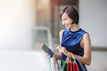 Portrait of young happy Asian woman holding mobile phone while shopping online through internet. Shopping online concept.