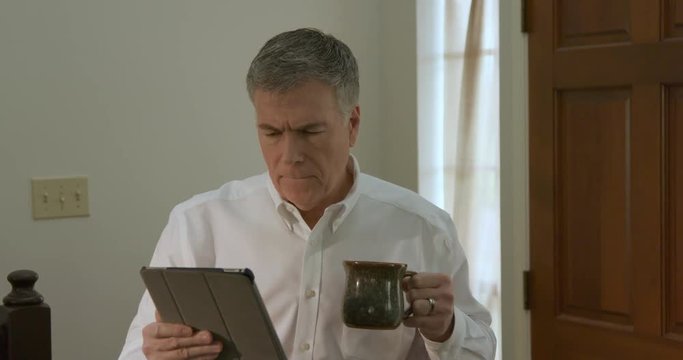 A serious businessman working from home looks at his tablet pc during a timeout for coffee. 4k