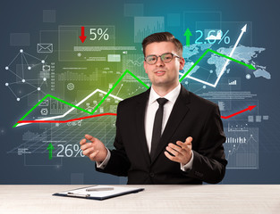 Young handsome businessman sitting at a desk with stocks and progress charts behind him